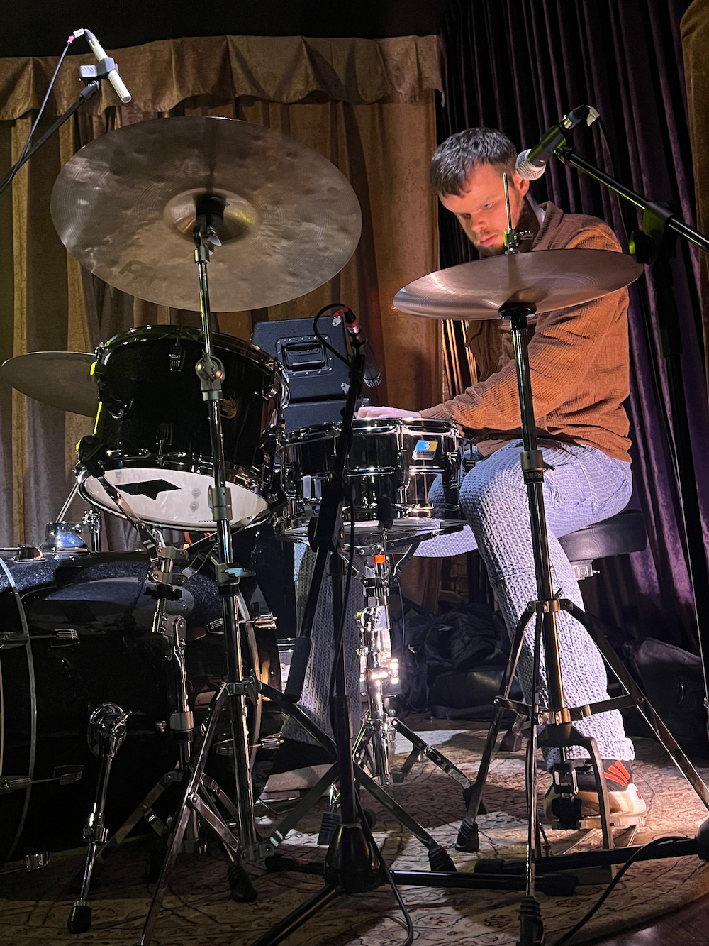 A White man with a beard plays the drums