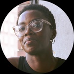 A headshot of a black woman with glasses, queer presenting with short black hair.