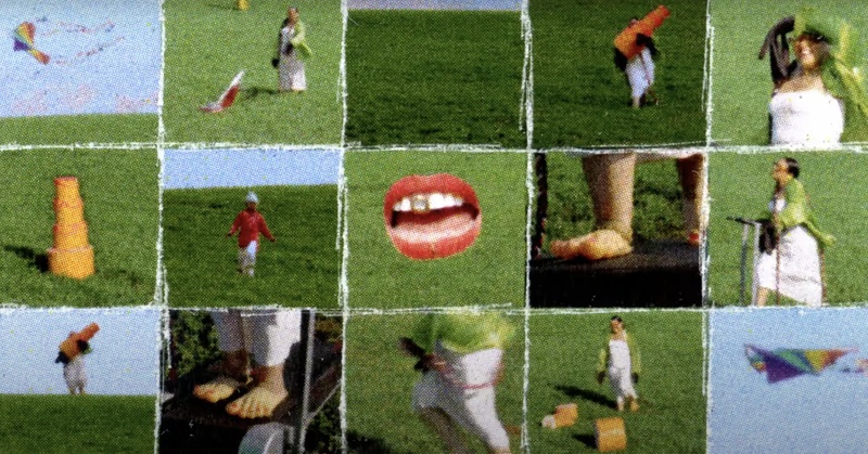  A still from a music video. There are fifteen squares each depicting a different image. Some are in the grass and some are in the air. Images range from kites to a performer moving around. 