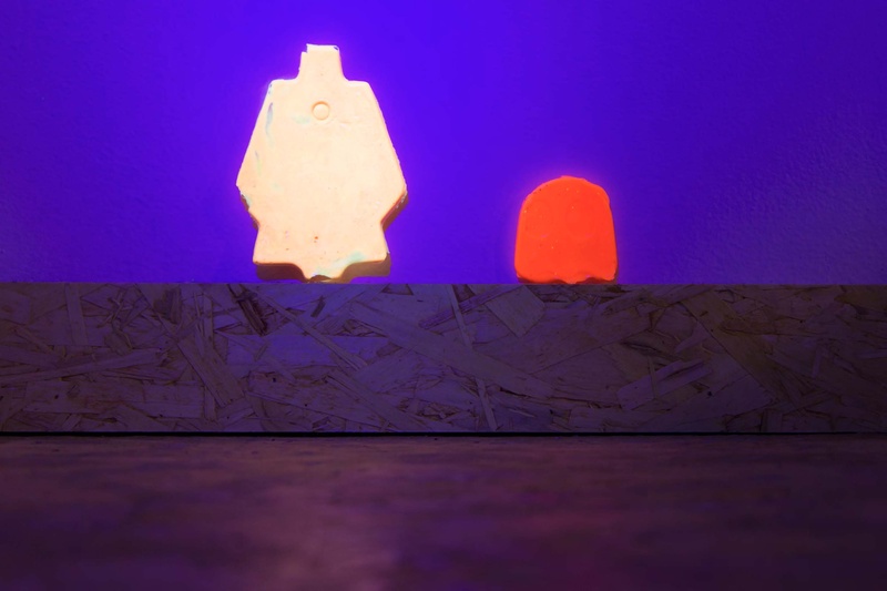  Two lighted figures mounted on purple wall. larger left figure glows white as smaller right image glows red 