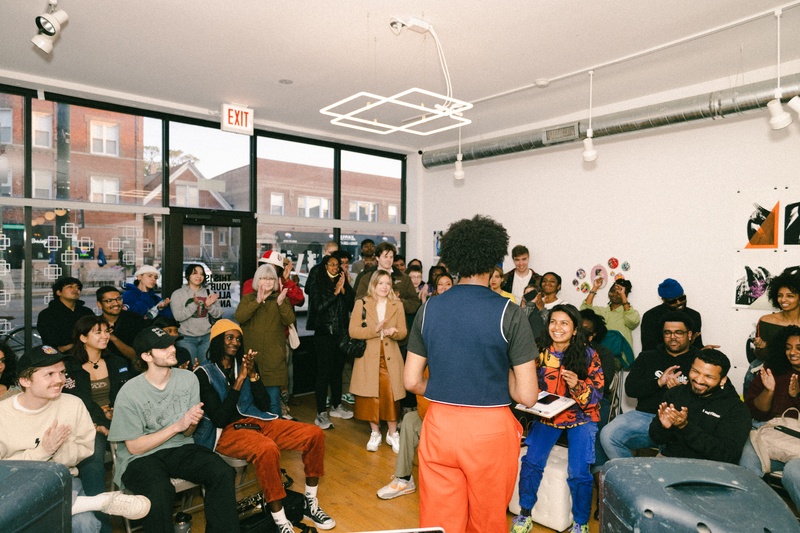  person with blue top and orange pants stands in front of crowd speaking 