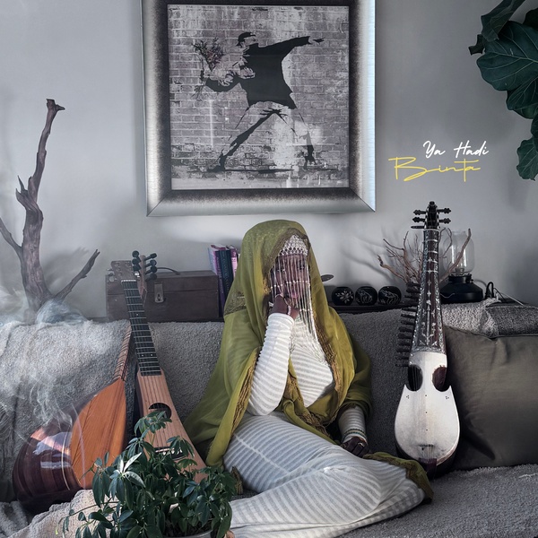  A Black Woman in a green Hijab sits on a couch. Next to her are two musical instruments. 