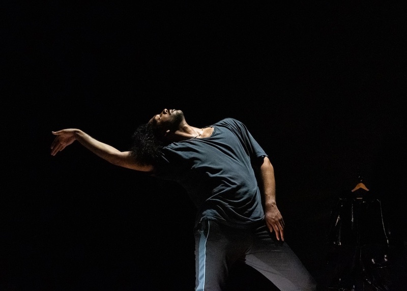  Light-skinned Black person with short black curly hair poses and they dance in an all black room 