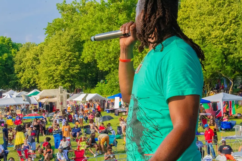  black man with locks and greenshots speaks into microphone facing a crowd 