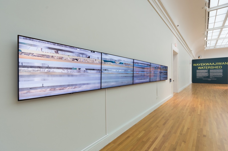  a row of five video monitors on a left side wall, with a large text reading "Watershed" opposite 