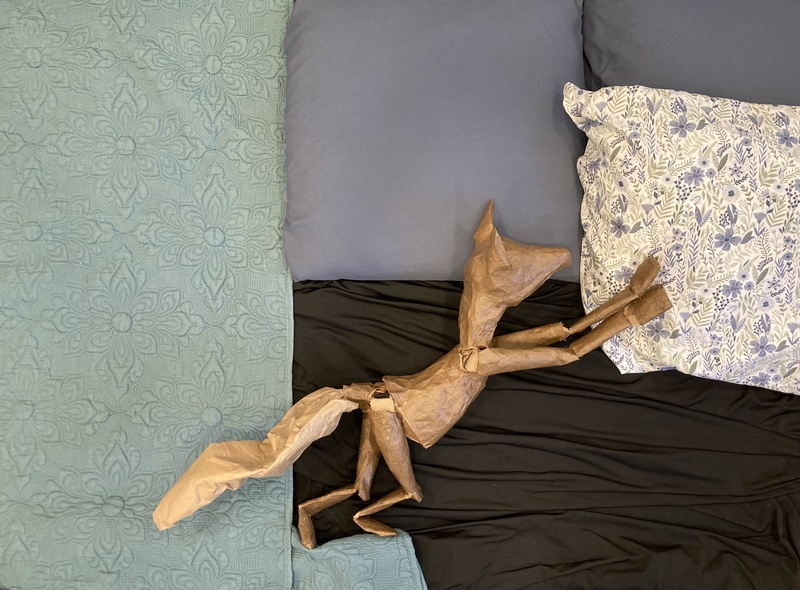  A paper puppet of a fox against a quilt and bedsheets. 