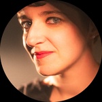 A headshot of a White femme presenting person with a short dark pixie cut.