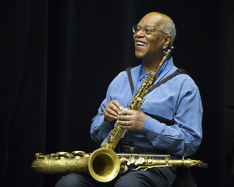  older black man holding holding two saxophones looks to the left 