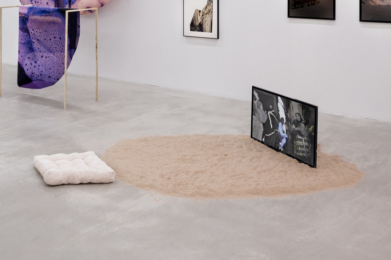  white cushion sits in front of television playing video. the tv sits on top of sand. 