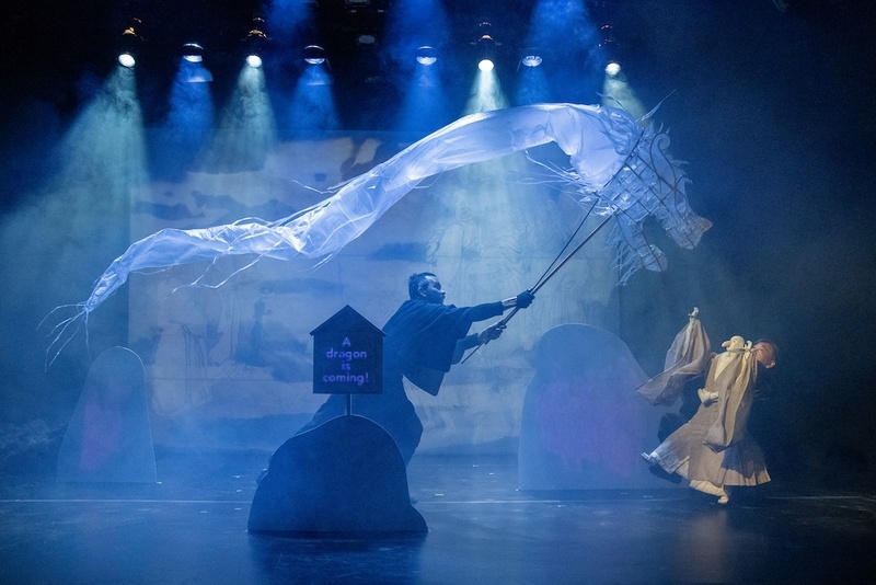  a biracial person with long black hair operates a large puppet of a water dragon. 