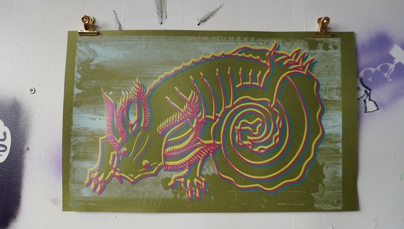  A screen printed illustration of a lizard like creature with axolotls features. The print is green with yellow and pink lines to highlight areas of the creature. 