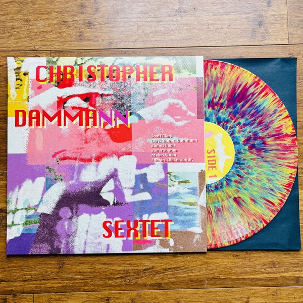  A photo of a vinyl record that has bright rainbow tie dye colors on the front. The cover reads Christopher Dammann Sextet 