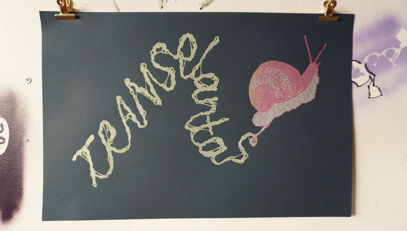  A silkscreen print on grey paper of a pink snake leaving a trail of slime that reads "Transplantas" 