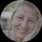 Older woman with dark salt and pepper hair, happy and smiling. Wearing a green T shirt and a silver dragon pendant.