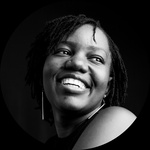A black and white headshot of a Black female artist with dark braids smiling.
