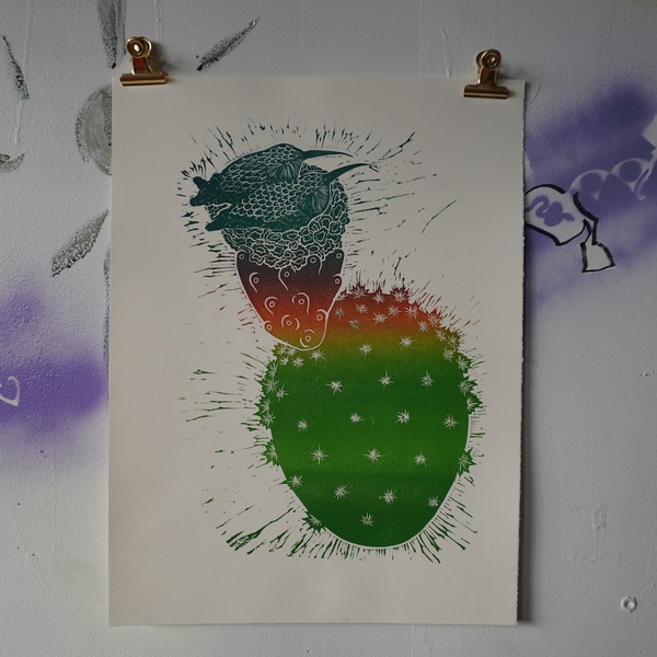  A block print of a cactus plant with a birds next perched on top. The cactus is green with a little orange. There are two birds in the nest. 