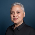 Headshot portrait of Laura Kina against a dark blue background. Laura has short white harir and is wearing a black shirt.