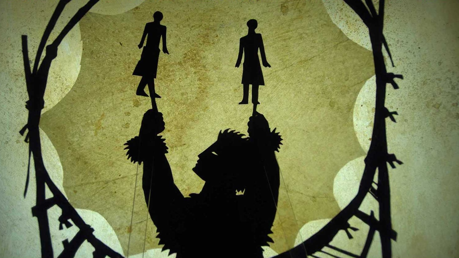 Image of a puppet behind a screen holding two human-like figures. A circular structure surrounds them and enscloses a star shape.